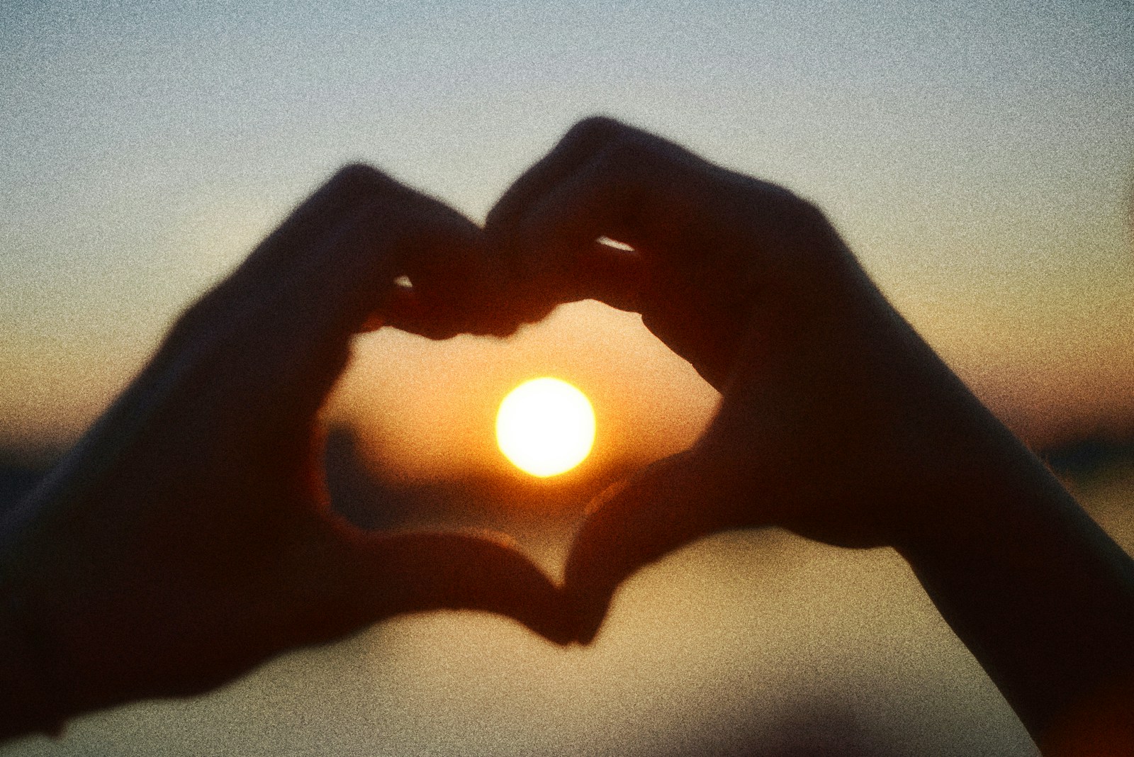 Hands forming a heart shape silhouetted against a beautiful sunset.